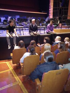 Young people sat on theatre chairs to talk to three people sat on a stage