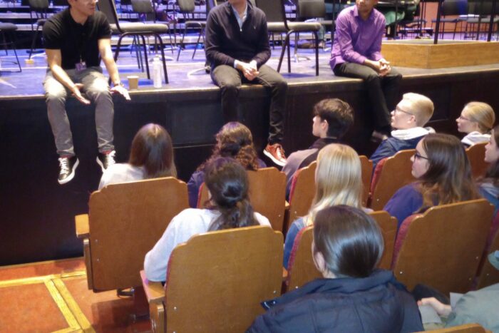 Young people sat on theatre chairs to talk to three people sat on a stage