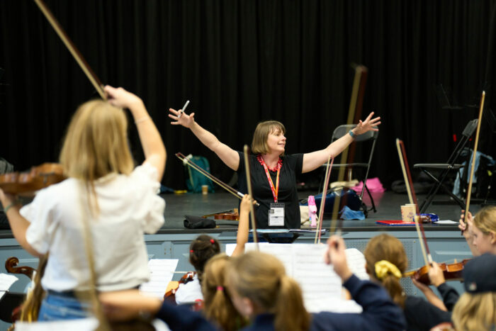 A woman conducts children playing stringed instruments