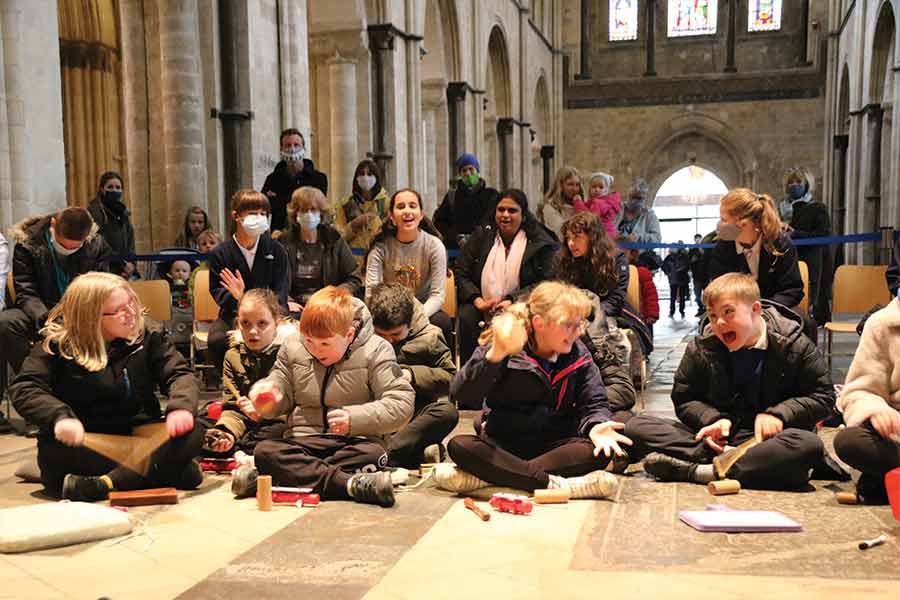 Five Children Sit In The Foreground, Cross Legged, Drawing In A Chapel