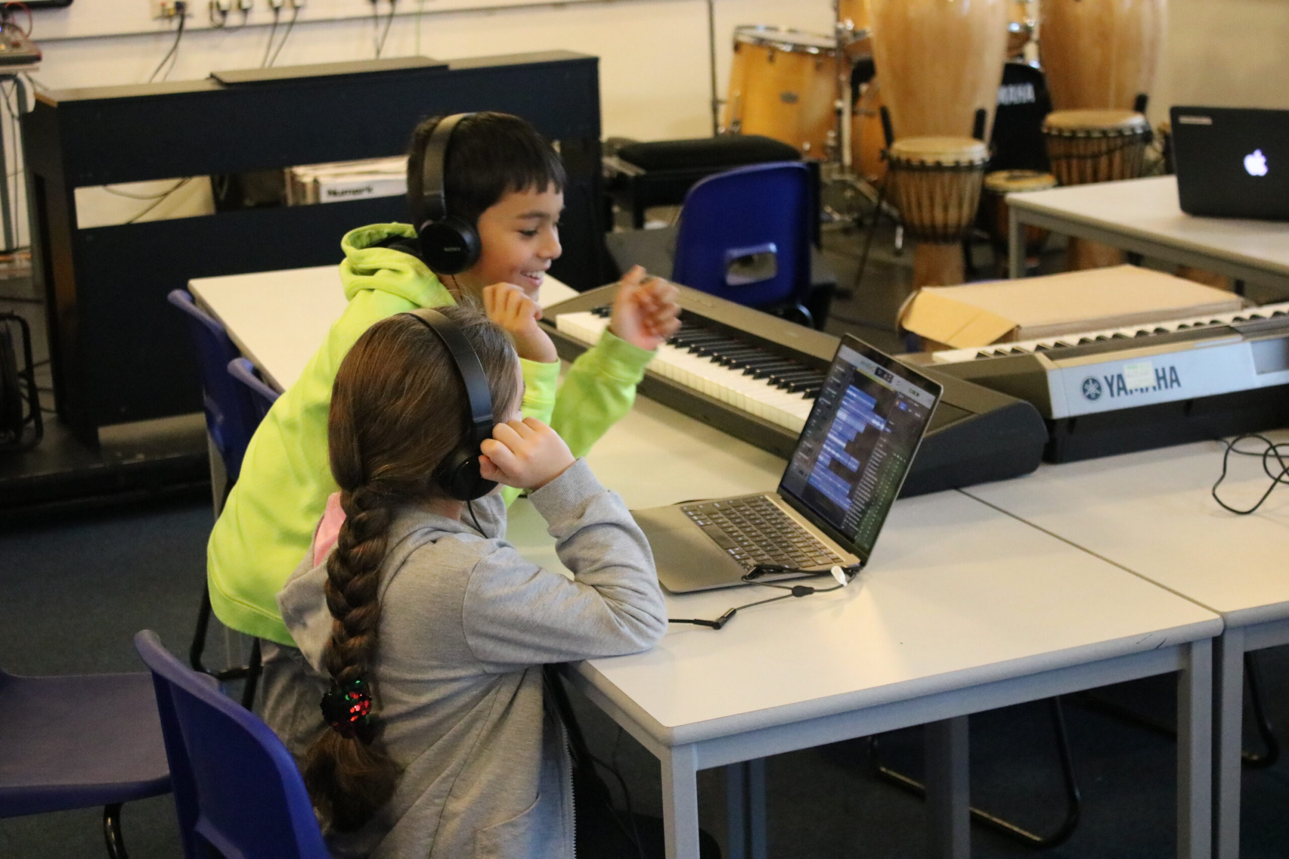 A Child In A Lime Green Hooded Sweatshirt Smiles With Another, Whilst Looking At A Computer