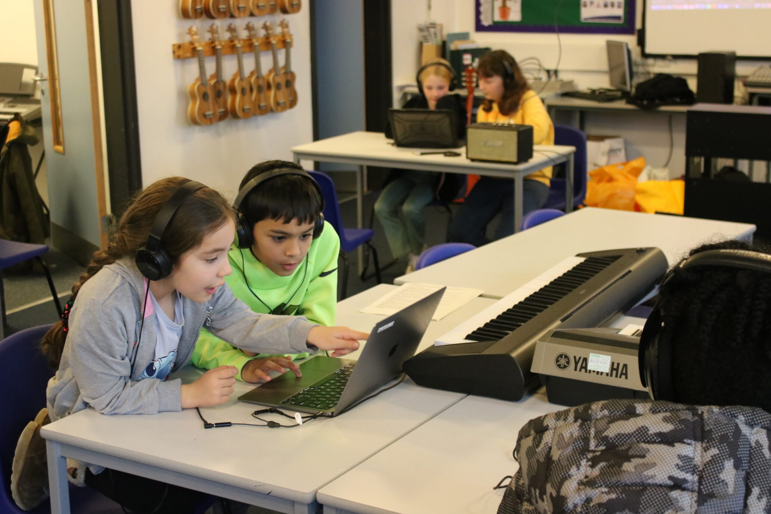 Two Children Work Together On A Computer, Two Others Are In The Background