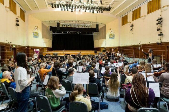 A group of young people sit performing as part of an orchestra