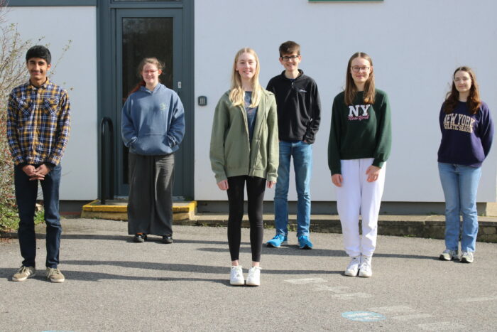 Six young people stand in front of a building