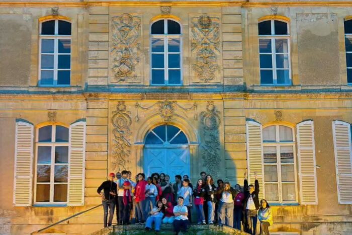 a grand building is lit up a group of young people stand in front of it