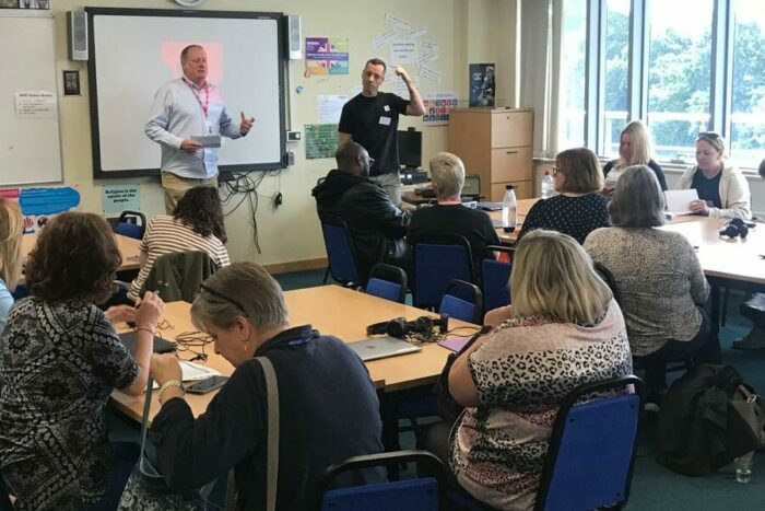 A group of adults sit in a classroom to learn from a teacher