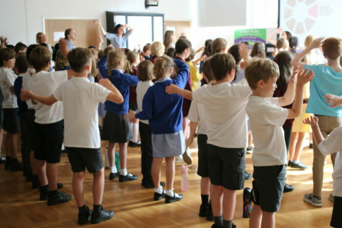 Children wave their arms and sing to a teacher
